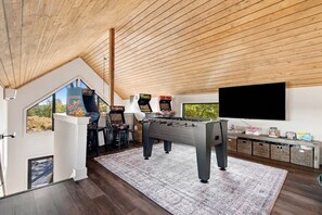 A modern room with a foosball table, a television, and a large window offering a view of the outdoors. - Views, Minigolf, Arcade, Sauna/Hot tub, New Aframe (Ellijay)