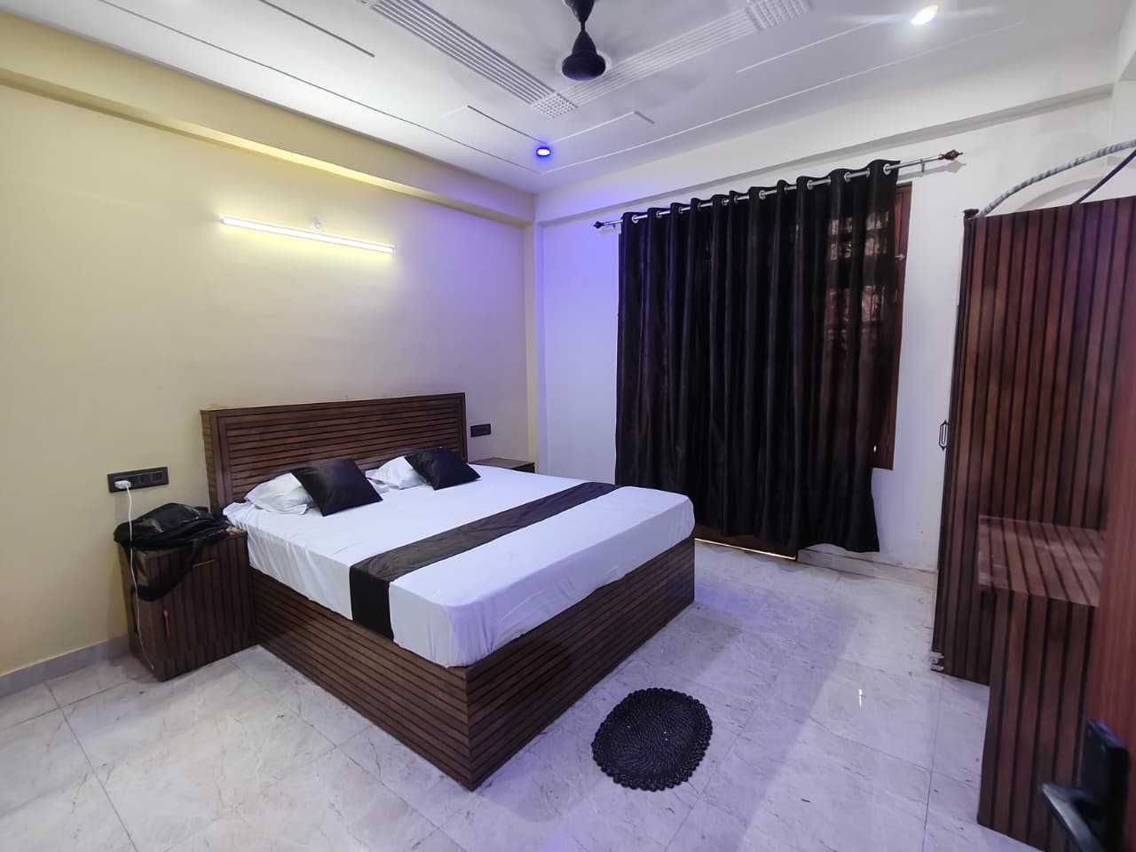 Une chambre moderne avec un grand lit, une table de chevet, une commode, un ventilateur de plafond et une fenêtre avec des rideaux.