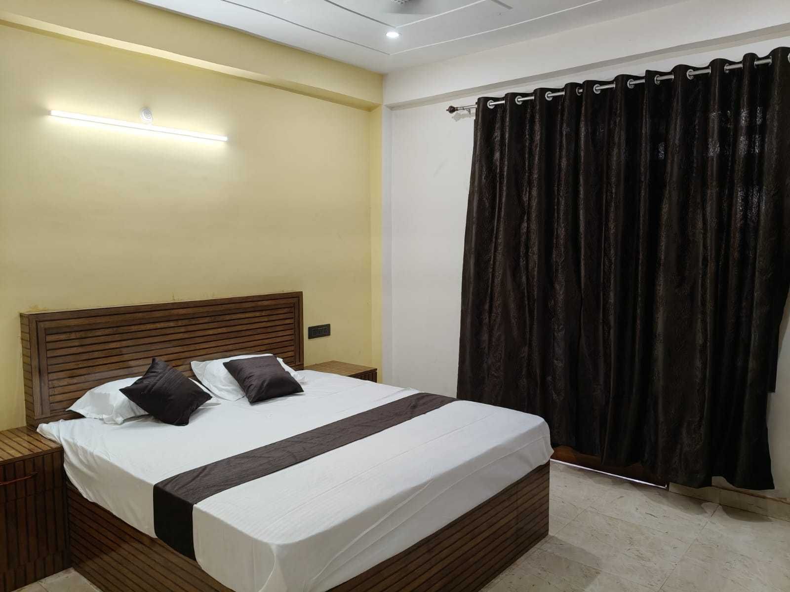 Une chambre d’hôtel avec un lit, des tables de chevet, une petite table, une lampe fixée au mur et un rideau.