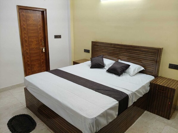 Un dormitorio con cama, dos mesitas de noche, cabecero de madera, una puerta con diseño floral y una alfombra redonda pequeña.