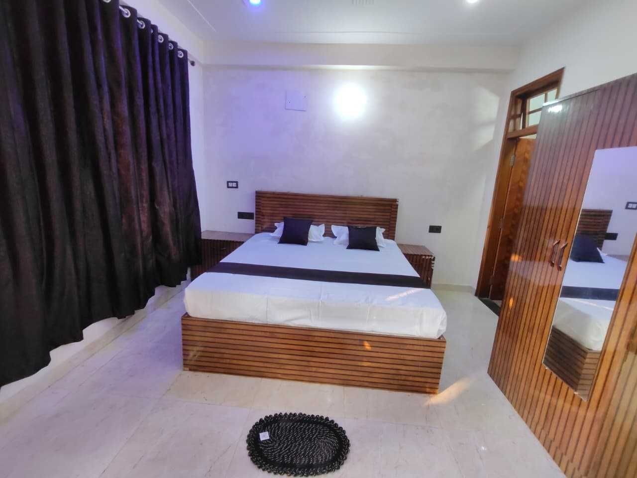 Une chambre avec un lit en bois, une table de chevet, un miroir et un tapis rond noir.