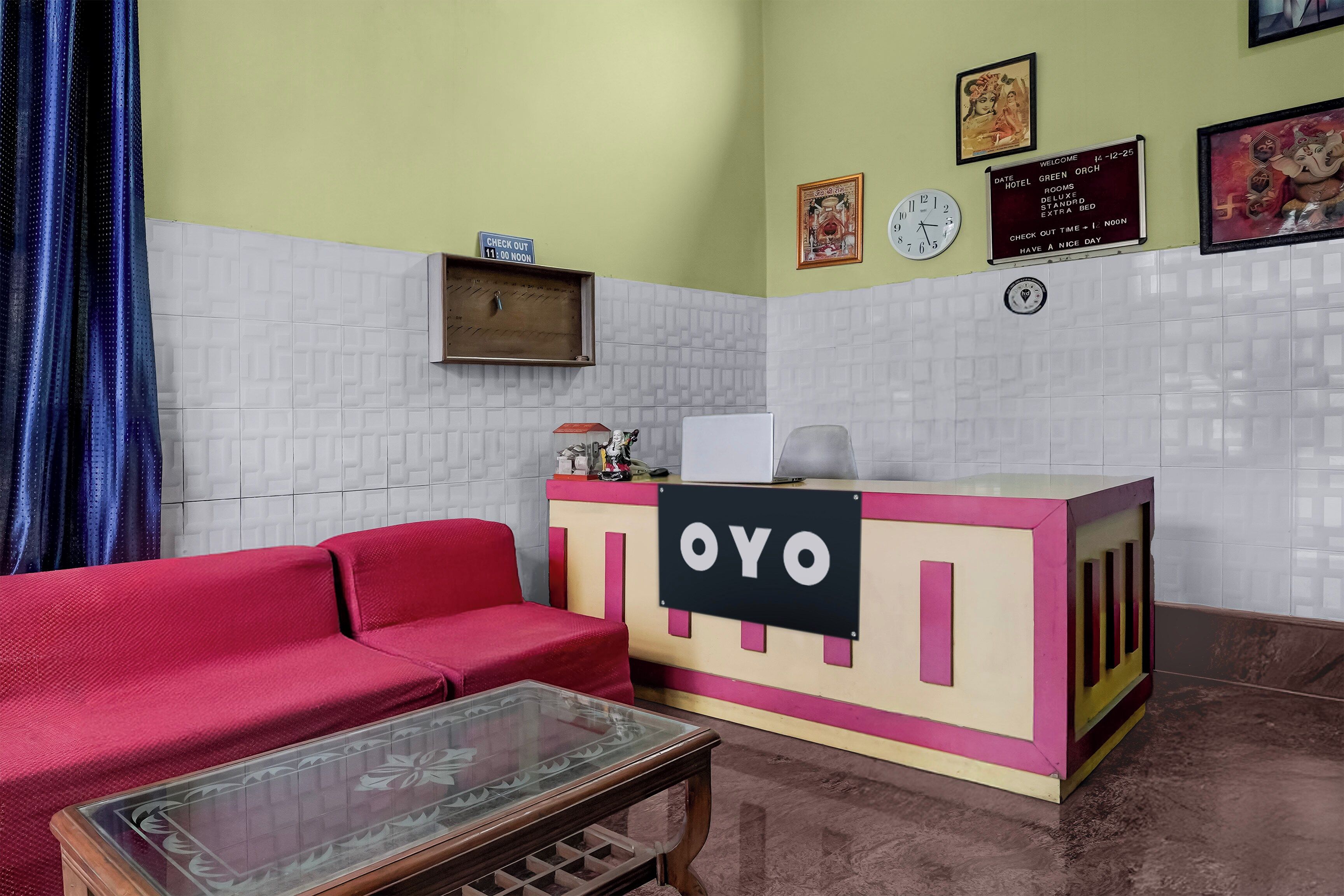 Bancada de recepção com placa indicando 'OYO' em saguão de hotel, com sofá vermelho e mesa de vidro.