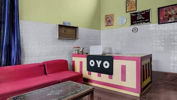 Bancada de recepção com placa indicando 'OYO' em saguão de hotel, com sofá vermelho e mesa de vidro.