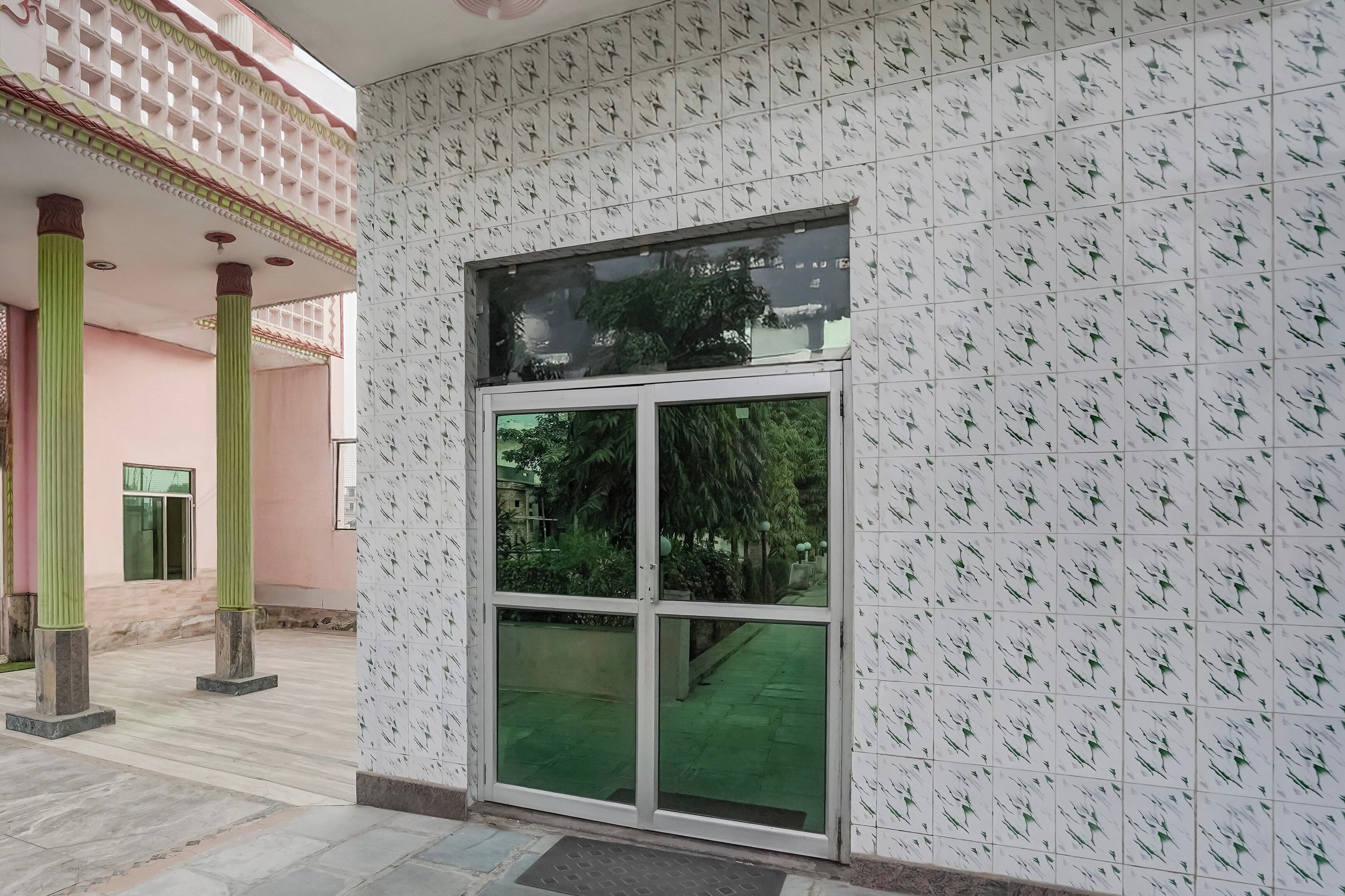 Entrada de um edifício com uma grande porta de vidro, paredes e chão revestidos de azulejos.