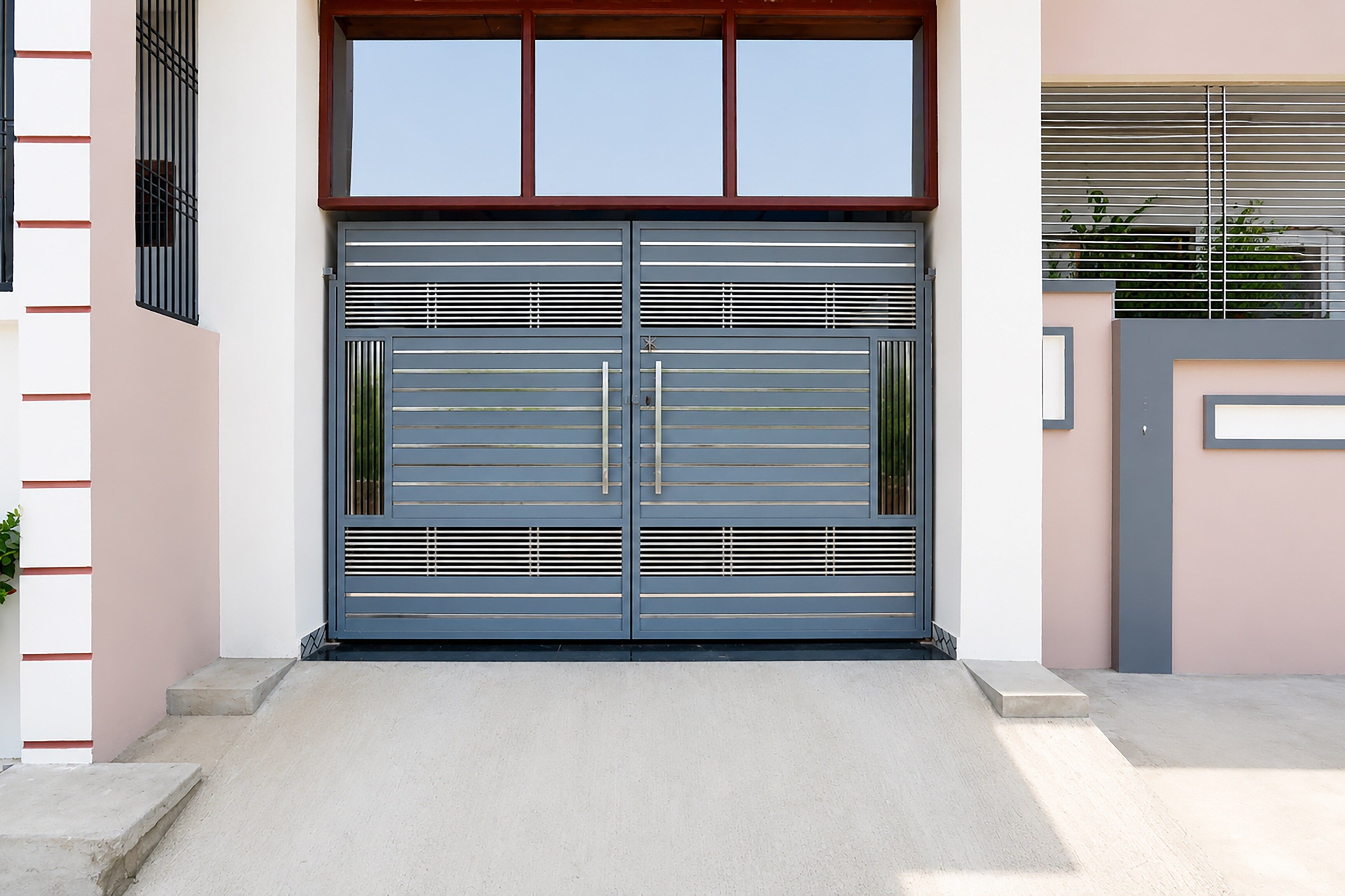 A modern building entrance with a double metal gate, a concrete ramp, and a small potted plant.