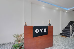En receptionsdisk med en skylt som visar texten ”OYO” i en modern byggnad med en trappa och ett golv med ett mönster.