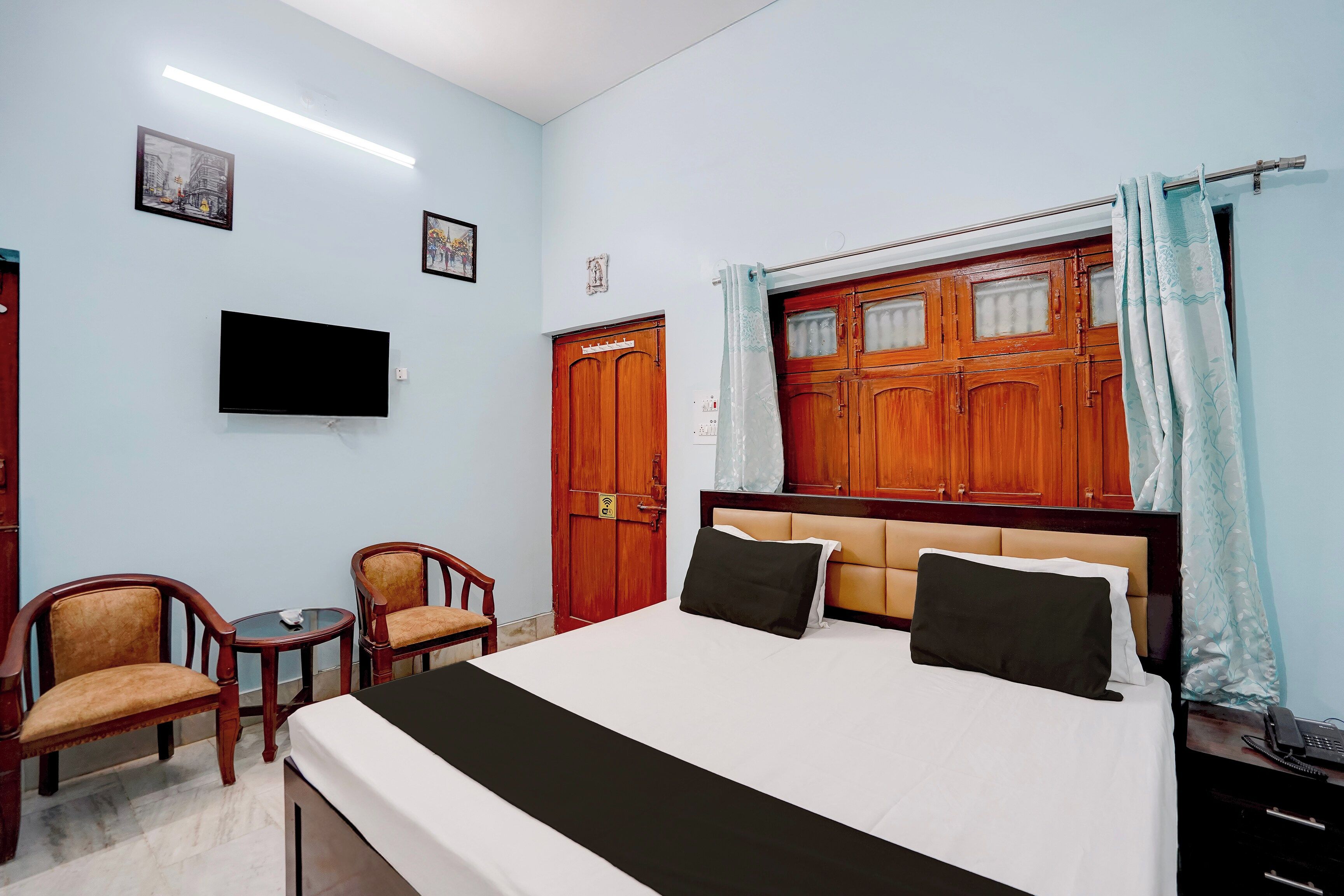 A hotel room with a bed, a television, a desk with a telephone, and two chairs.