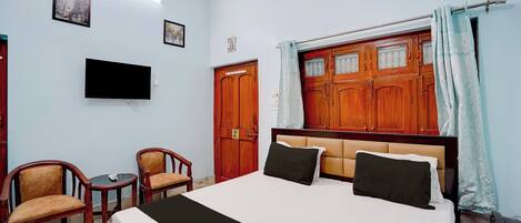 A hotel room with a bed, a television, a desk with a telephone, and two chairs.