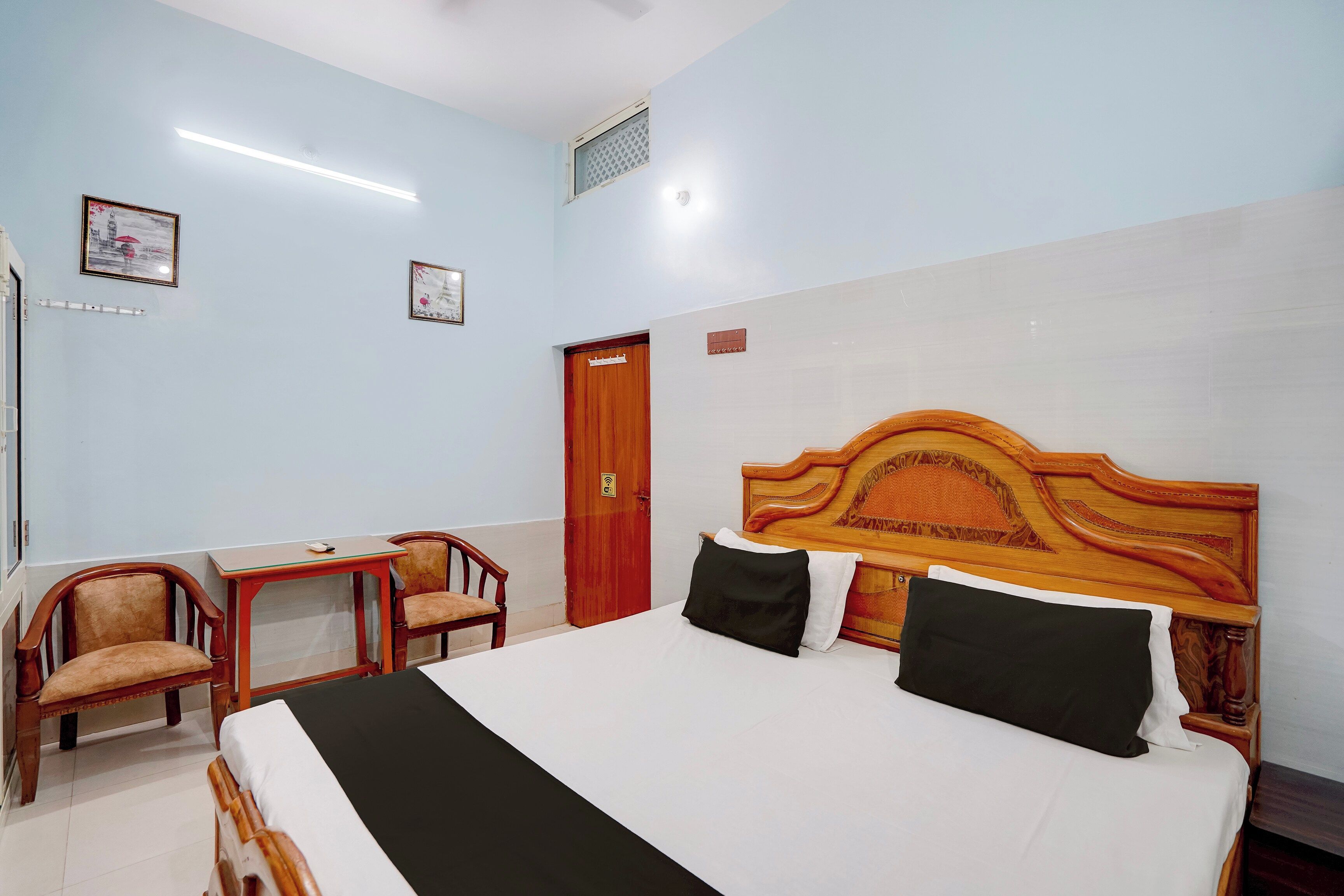 Habitación de hotel con una cama grande, un escritorio, dos sillas, una puerta de madera y una lámpara en el techo.