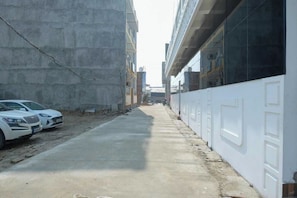 Un carrer estret amb una paret de formigó a un costat i un edifici blanc a l'altre. Hi ha dos cotxes blancs estacionats al costat de la paret.