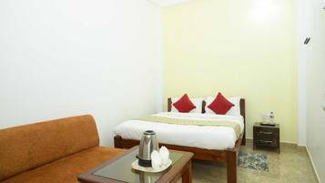 A hotel room with a bed, a sofa, a bedside table with a kettle, and a nightstand.