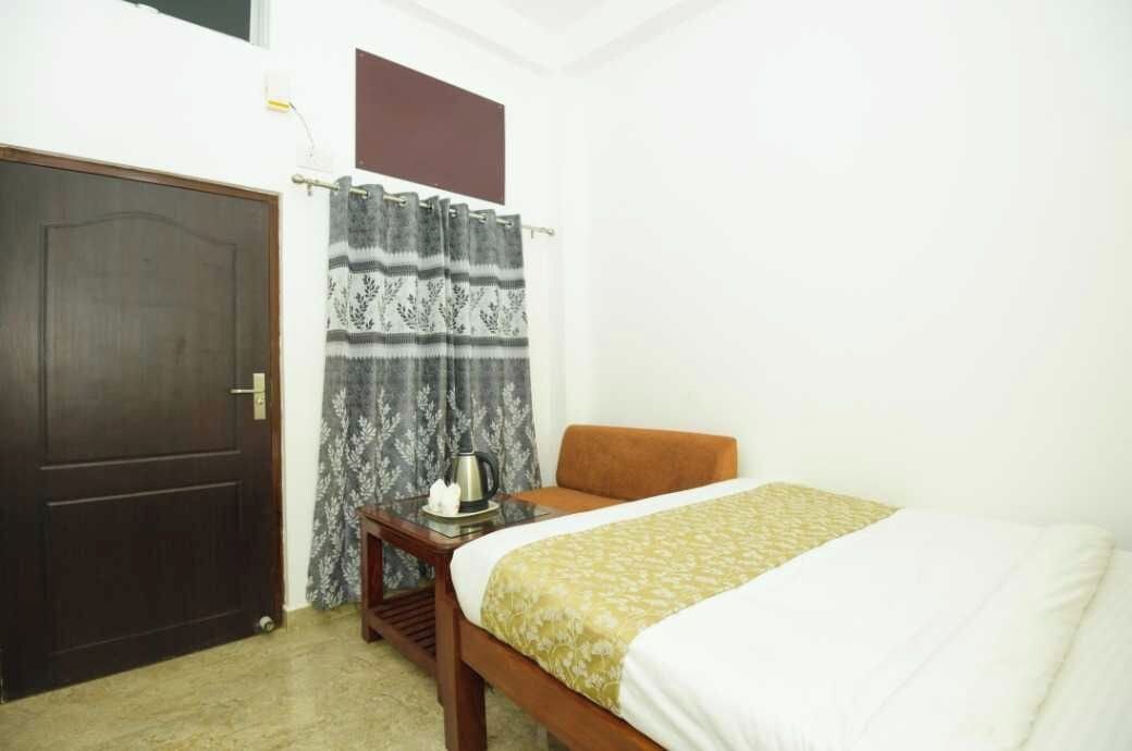 Quarto com cama, mesa de cabeceira de madeira, chaleira e cortina.