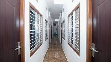 Corredor com portas e janelas de madeira e grades de metal, que leva a um quarto com piso ladrilhado.