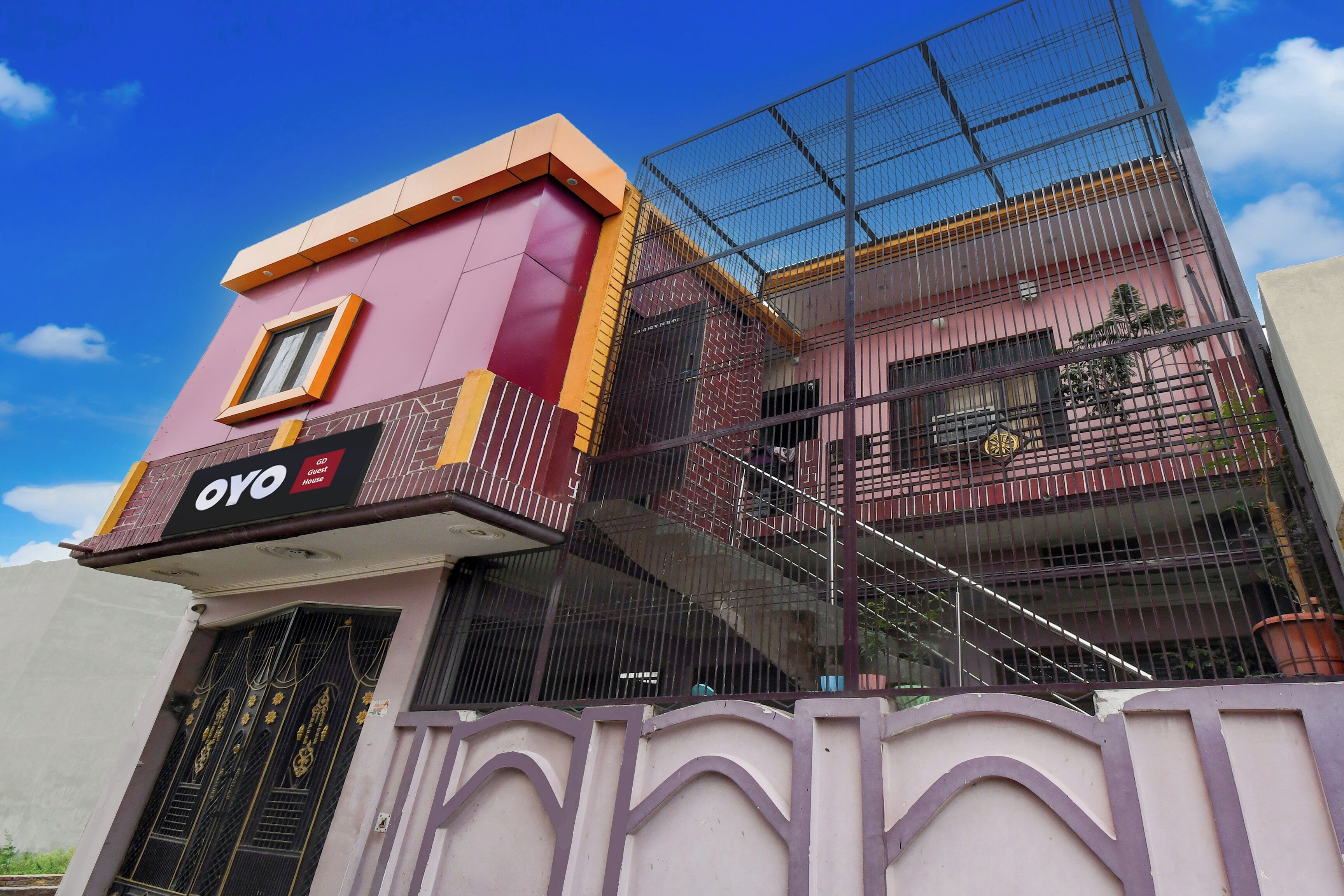 A multi-story building with a prominent 'GO Guest House' sign, a balcony with a metal railing, and a staircase leading to the upper floors.