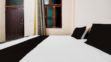 A room with a bed, a door, a window, and a wall-mounted light fixture.