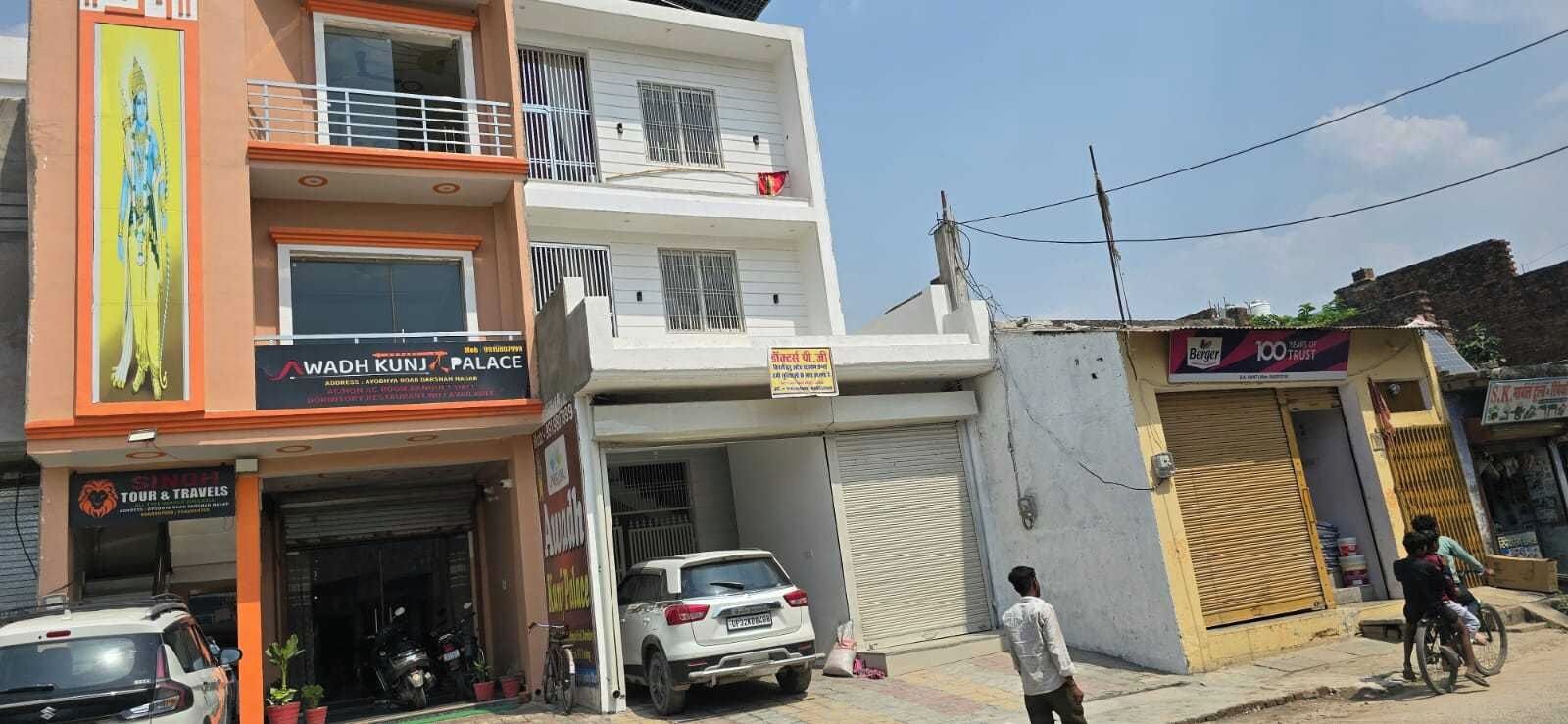 A multi-story building with a sign for 'WADH KUNJ PALACE' and a closed shop with a sign for '100 TRUST'.
