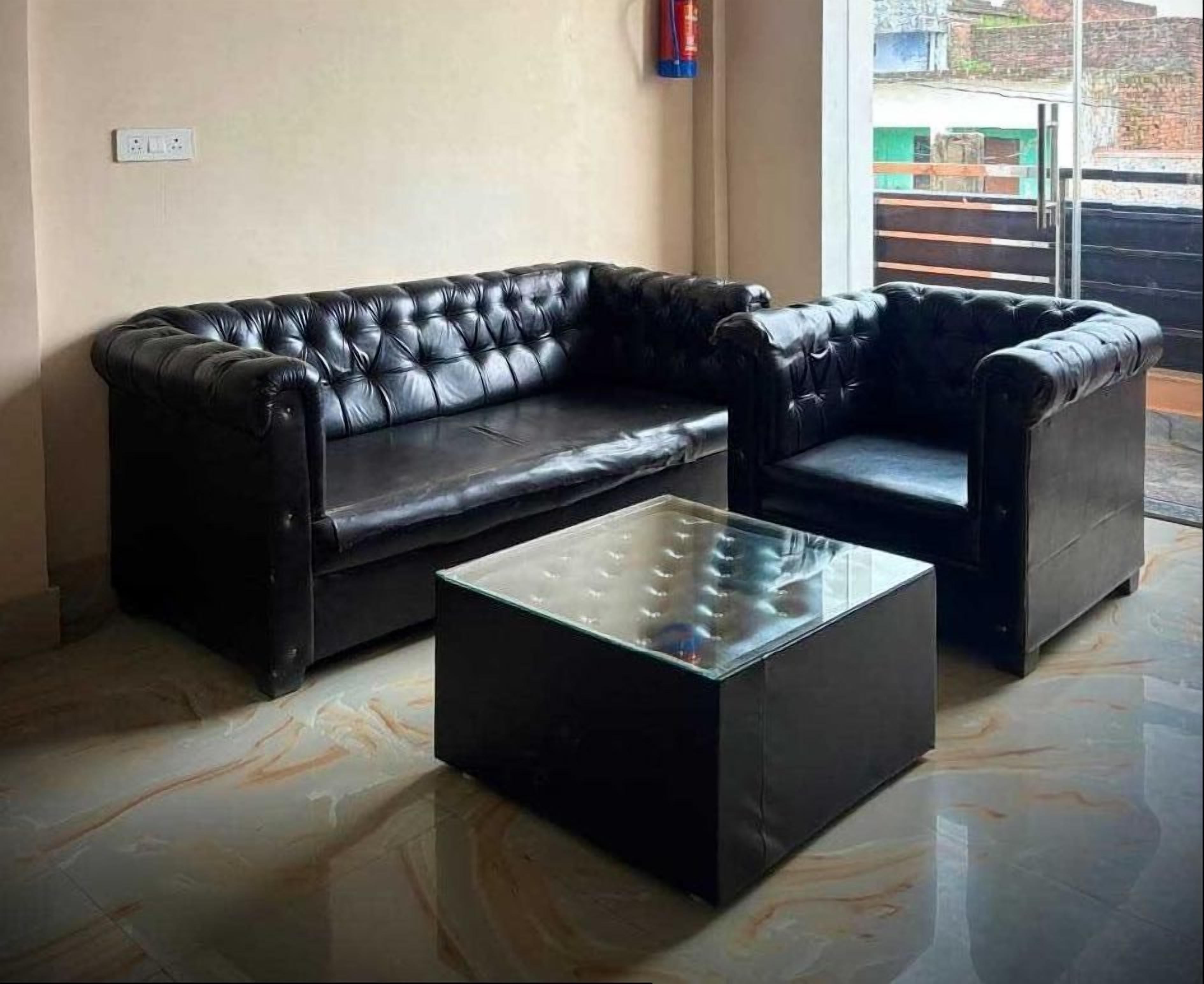 A black leather sofa set with a glass-top coffee table in a room with a tiled floor and a window with a view of buildings.