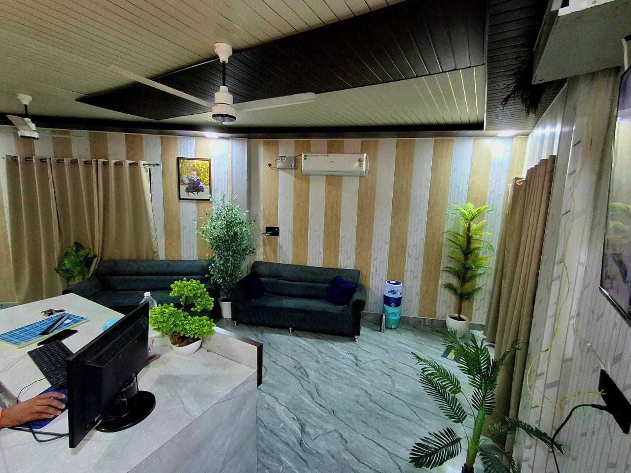 A reception area with a desk, computer, sofa, and potted plants.