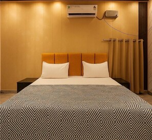 Ett hotellrum med en säng, en sänggavel, en luftkonditioneringsanläggning och gardiner.