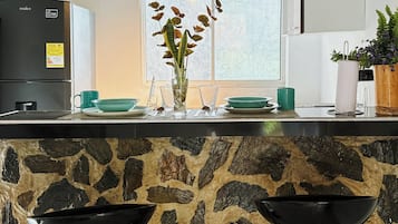 A kitchen with a stone countertop, two black bar stools, a refrigerator, and a window with a view.