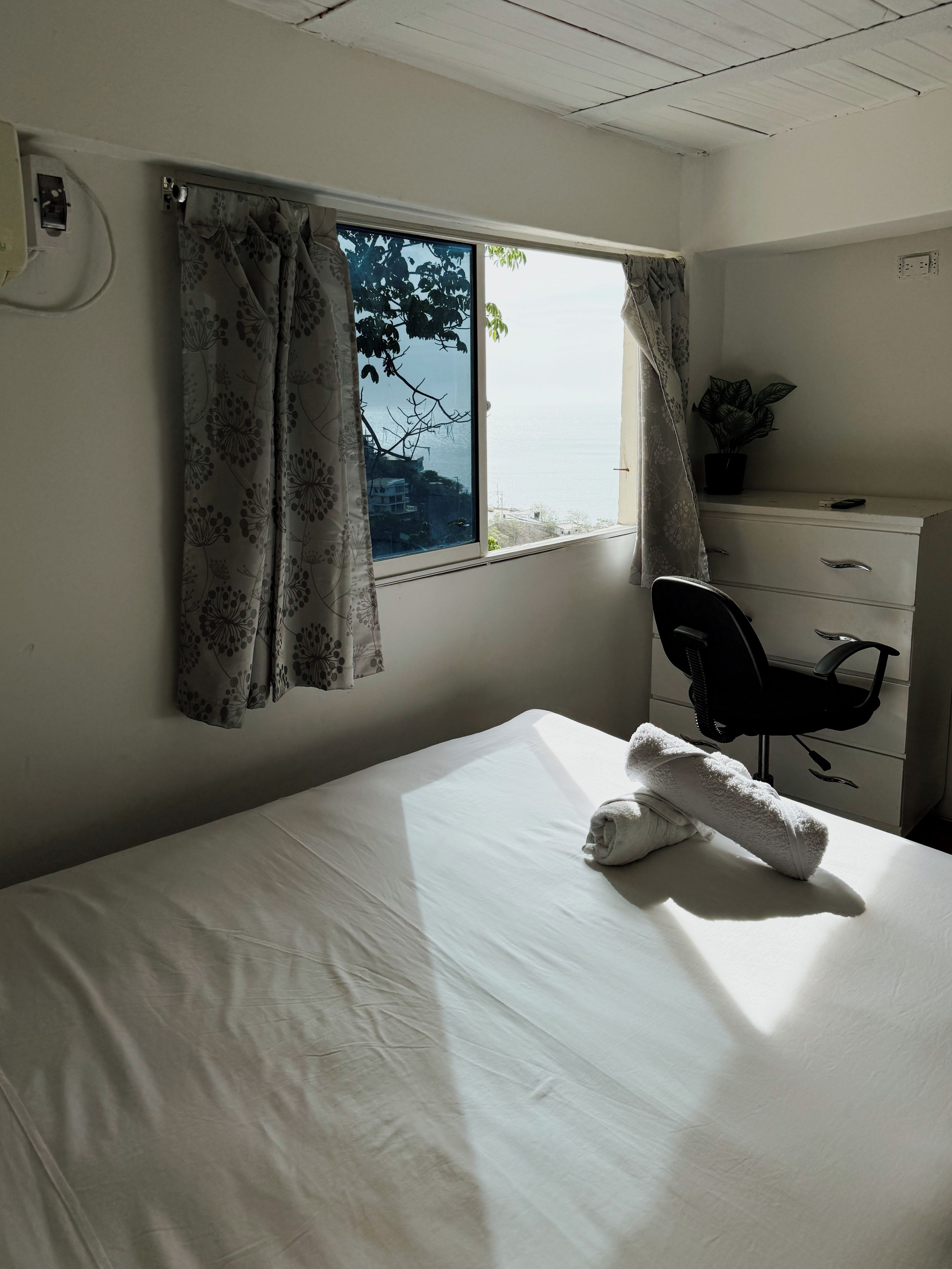 A hotel room with a bed, a desk, a chair, a dresser, and a window with curtains.