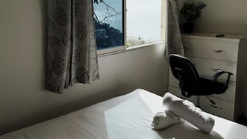 A hotel room with a bed, a desk, a chair, a dresser, and a window with curtains.