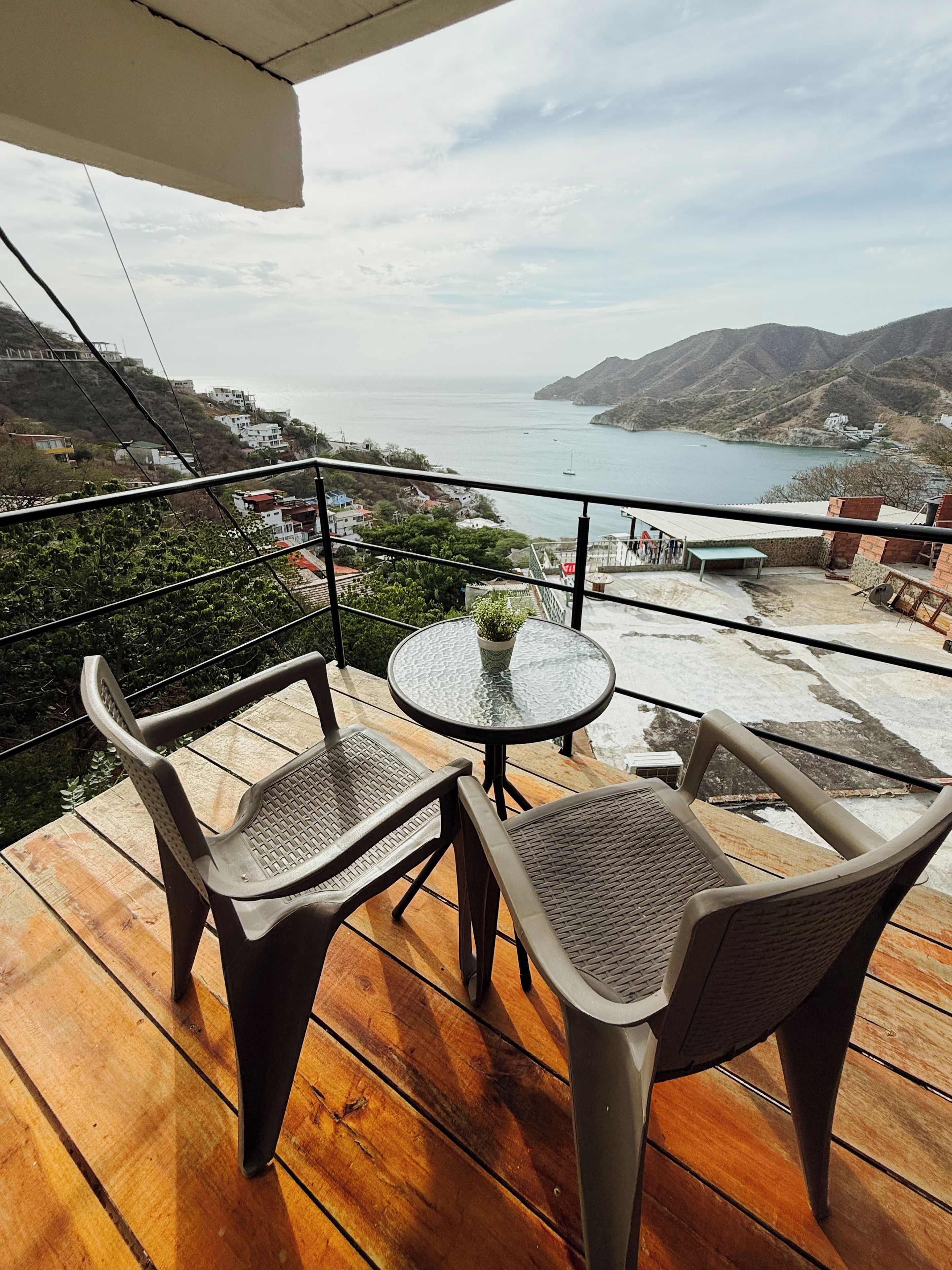 A wooden deck with two chairs and a table, overlooking a coastal landscape with hills and a body of water.