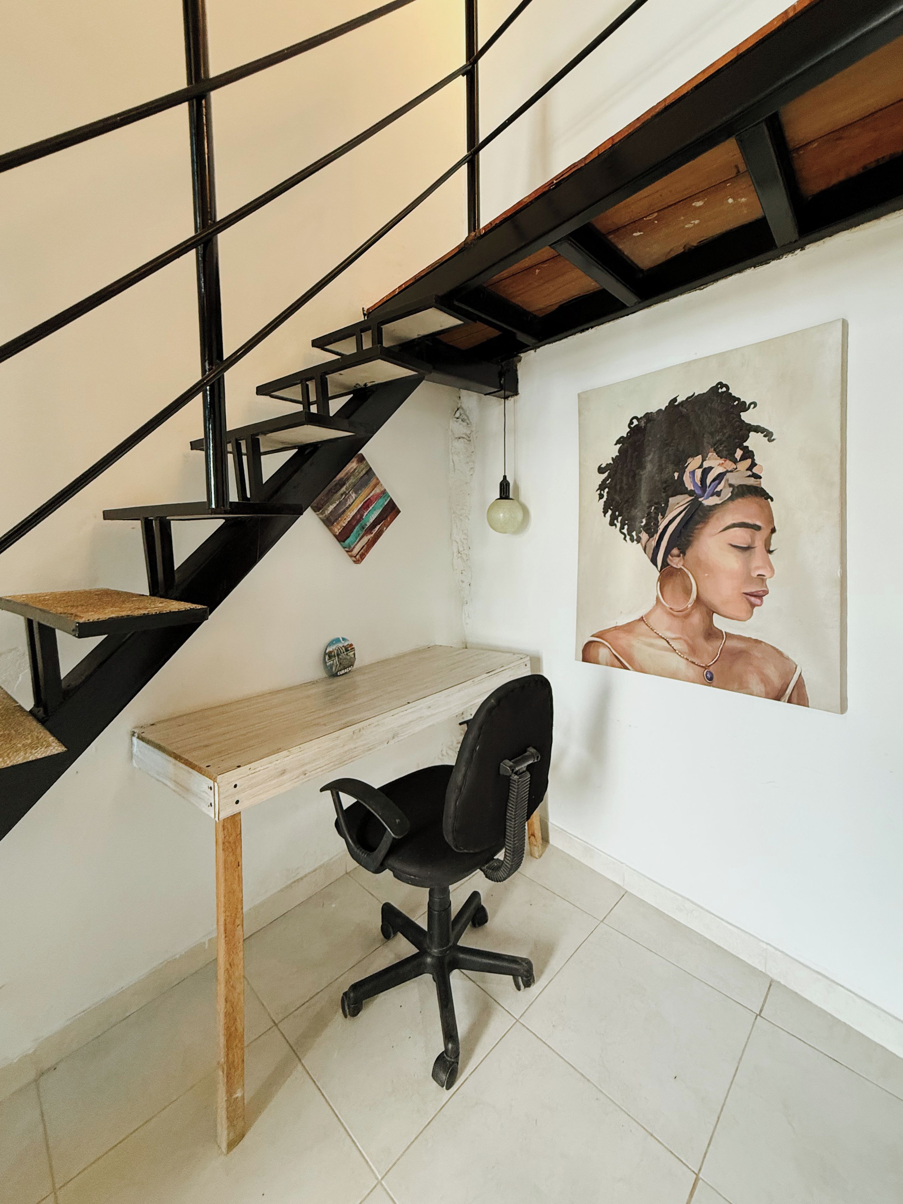 A staircase with a black metal railing, a wooden desk, a black office chair, and a framed portrait on the wall.