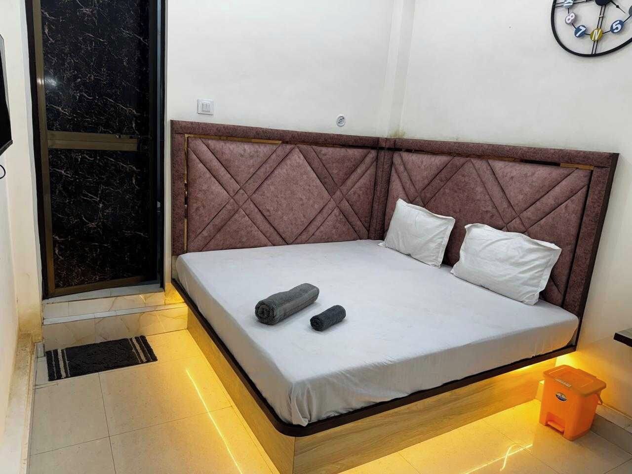 A single bed with a padded headboard, a bedside table, and a wall clock.