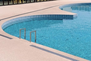 Una piscina con borde curvo y dos escaleras de metal.