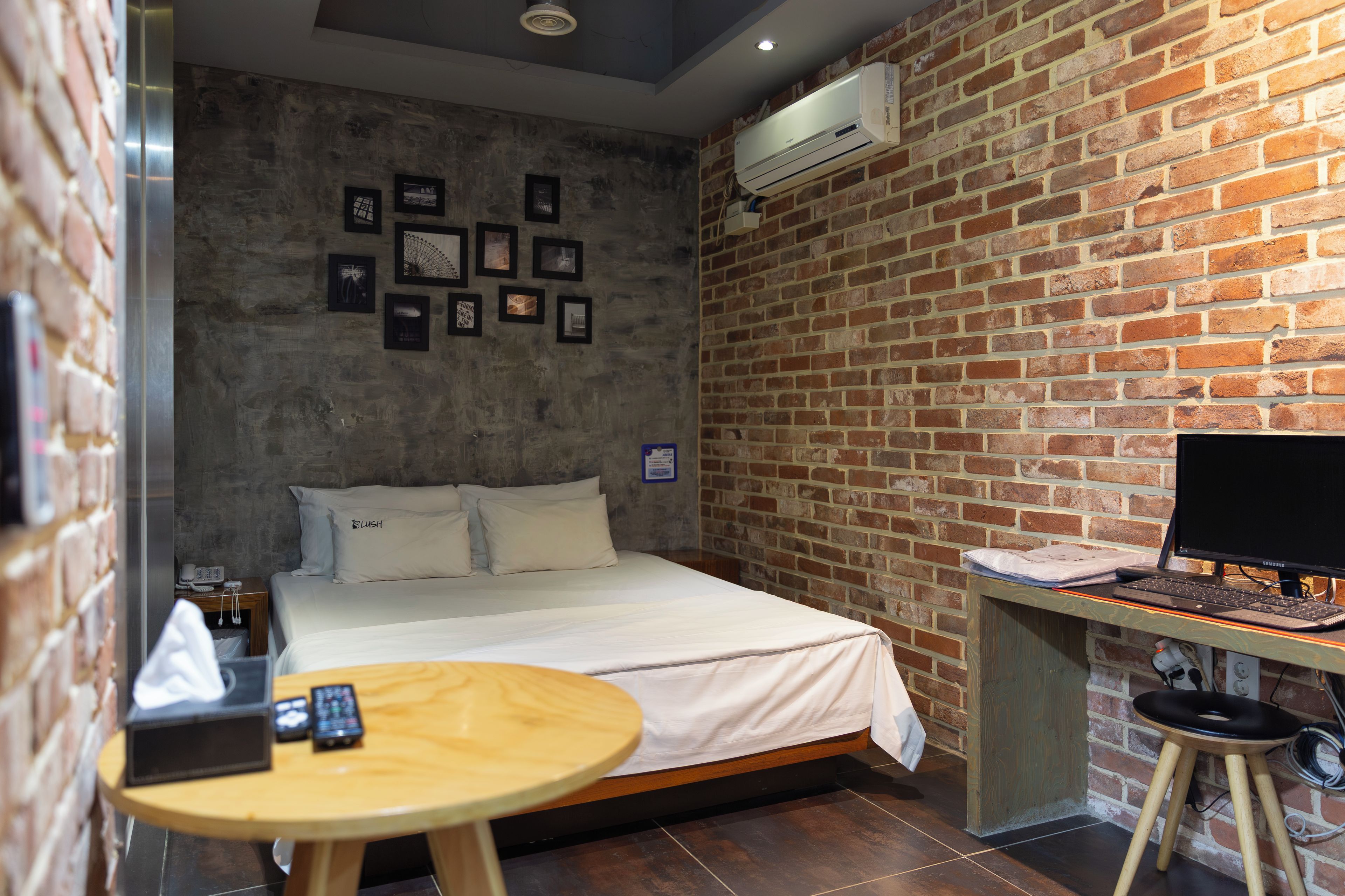 Une chambre d’hôtel avec un lit, un bureau équipé d’un ordinateur, une table ronde et un mur en briques orné de tableaux.