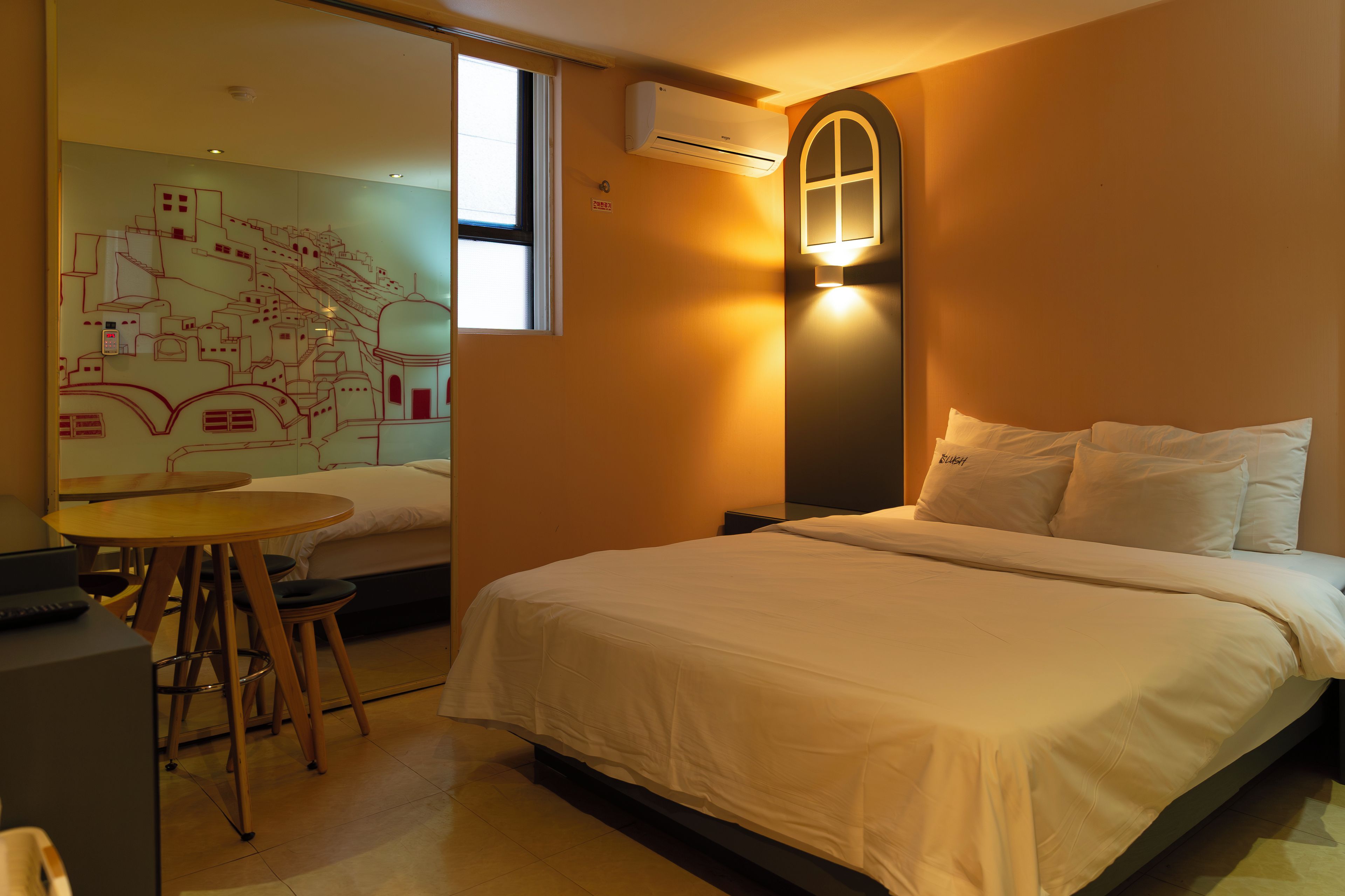 Une chambre d’hôtel comprenant un lit, un bureau avec une chaise, un climatiseur fixé au mur et une fenêtre.