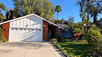 Une maison à deux étages avec un garage, une pelouse bien entretenue et une variété d’arbres et d’arbustes.