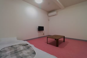 A room with a bed, a small table, an air conditioning unit, and a wall-mounted television. - Smart House Miduho (Kuma District Nishiki)