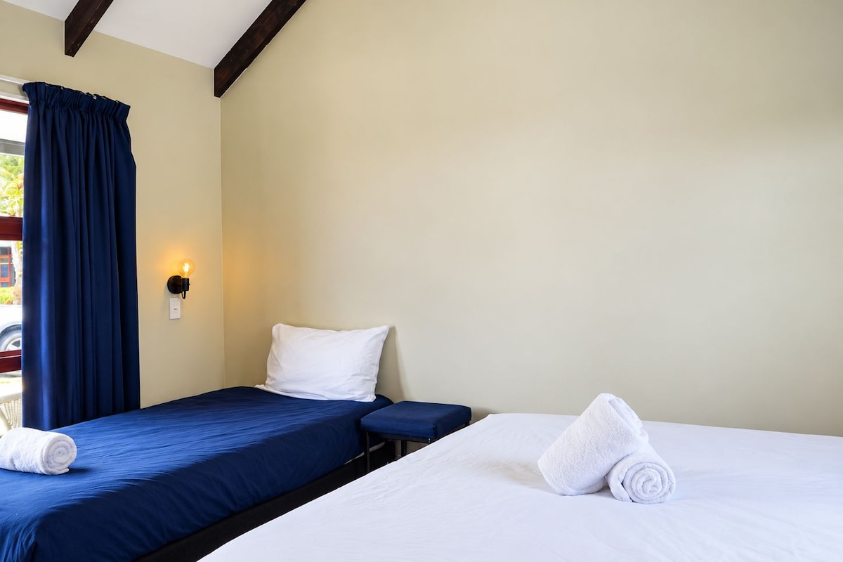 A hotel room with two beds, one with a blue bedspread and the other with a white bedspread.
