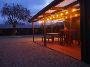 A reception area with a wooden bench and table, surrounded by a covered outdoor space with string lights. - 27 Cron Street (Franz Josef/Waiau)