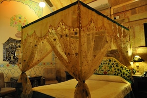 Habitació amb un llit cobert per un dosser floral, una paret decorativa i un capçal de llit amb dibuixos.