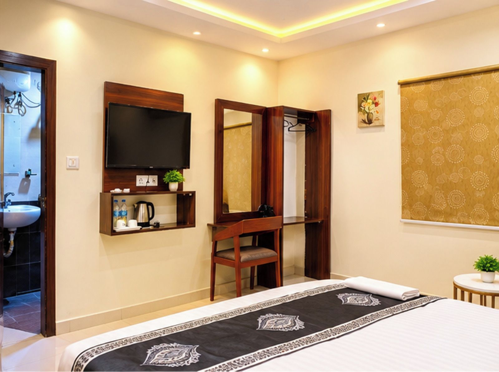 Habitación de hotel con cama, televisor, espejo, lavamanos y una pequeña mesa con una planta.