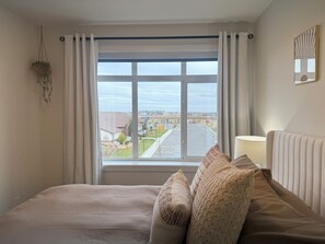 Habitación de hotel con una ventana grande, una cama con almohadas, una lámpara de noche y una planta colgante.
