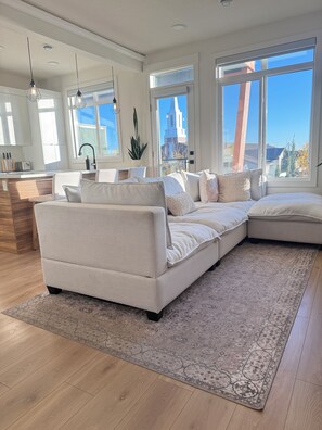 Una sala de estar moderna con un sofá modular, una cocina y ventanas amplias que ofrecen vistas de la ciudad.