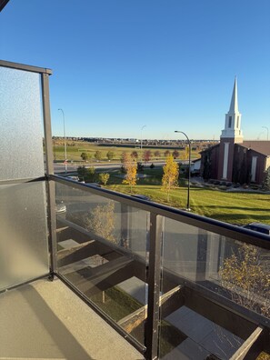 Vista desde un balcón con cielo despejado, una aguja de iglesia y un estacionamiento.