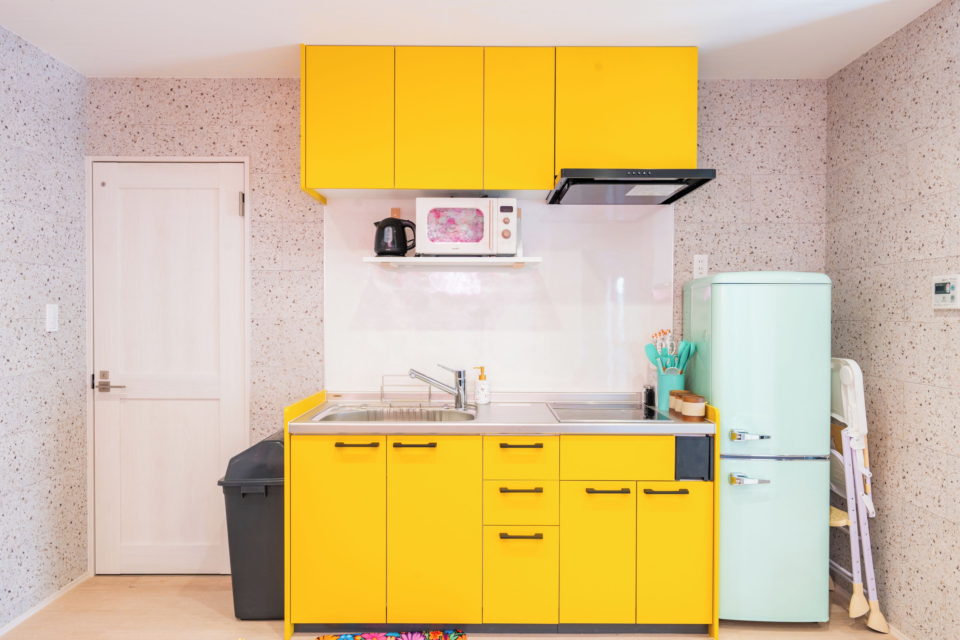 A compact kitchen with yellow cabinets, a microwave, a sink, and a small refrigerator.