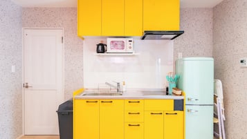 A compact kitchen with yellow cabinets, a microwave, a sink, and a small refrigerator.