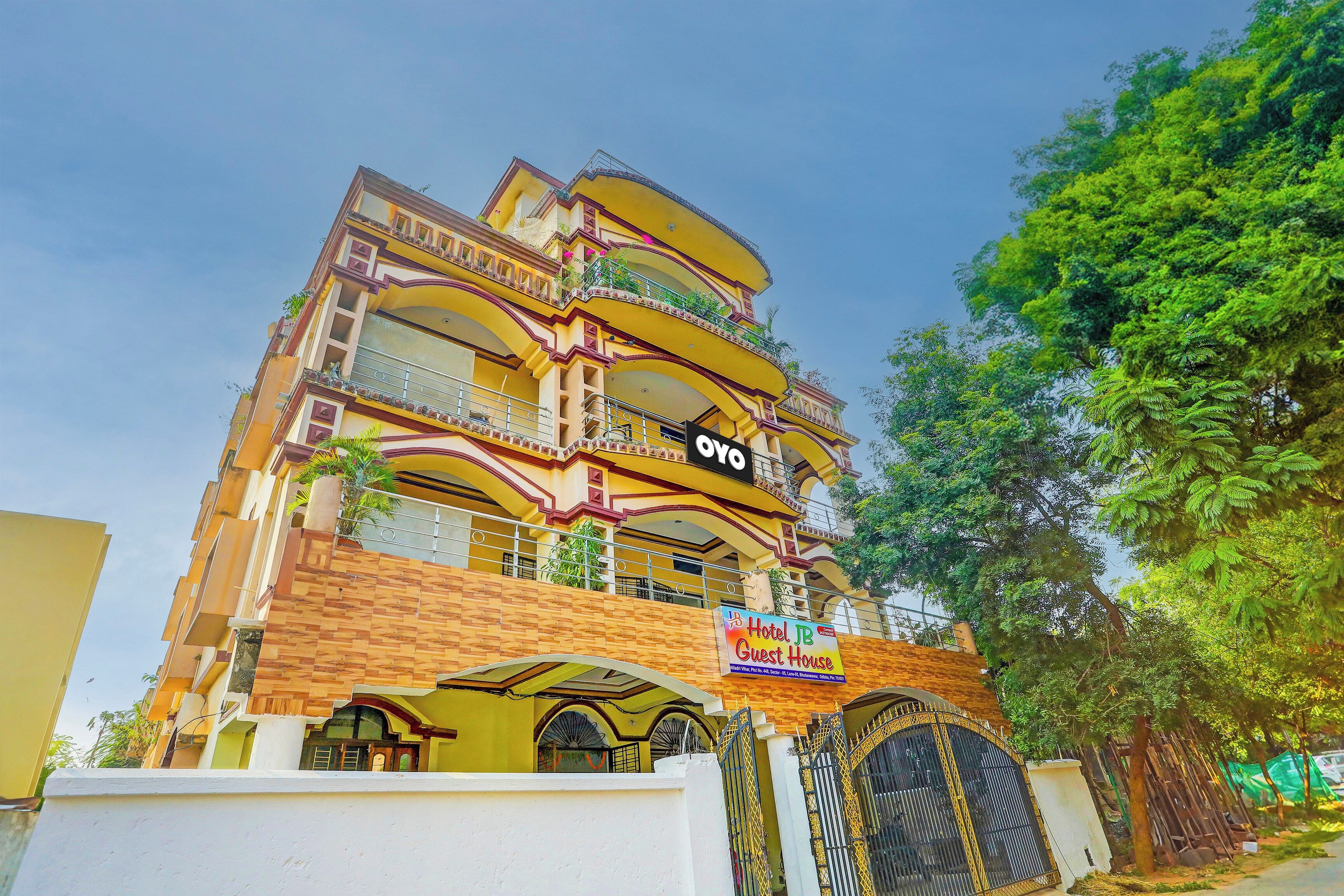 Un hotel de varios pisos con balcones, un letrero que indica 'Hotel JB Guest House' y una entrada con portón.