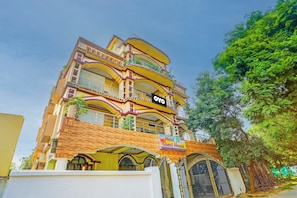 Un hôtel à plusieurs étages doté de balcons, une enseigne indiquant « Hôtel JB Guest House », et une entrée fermée par un portail.