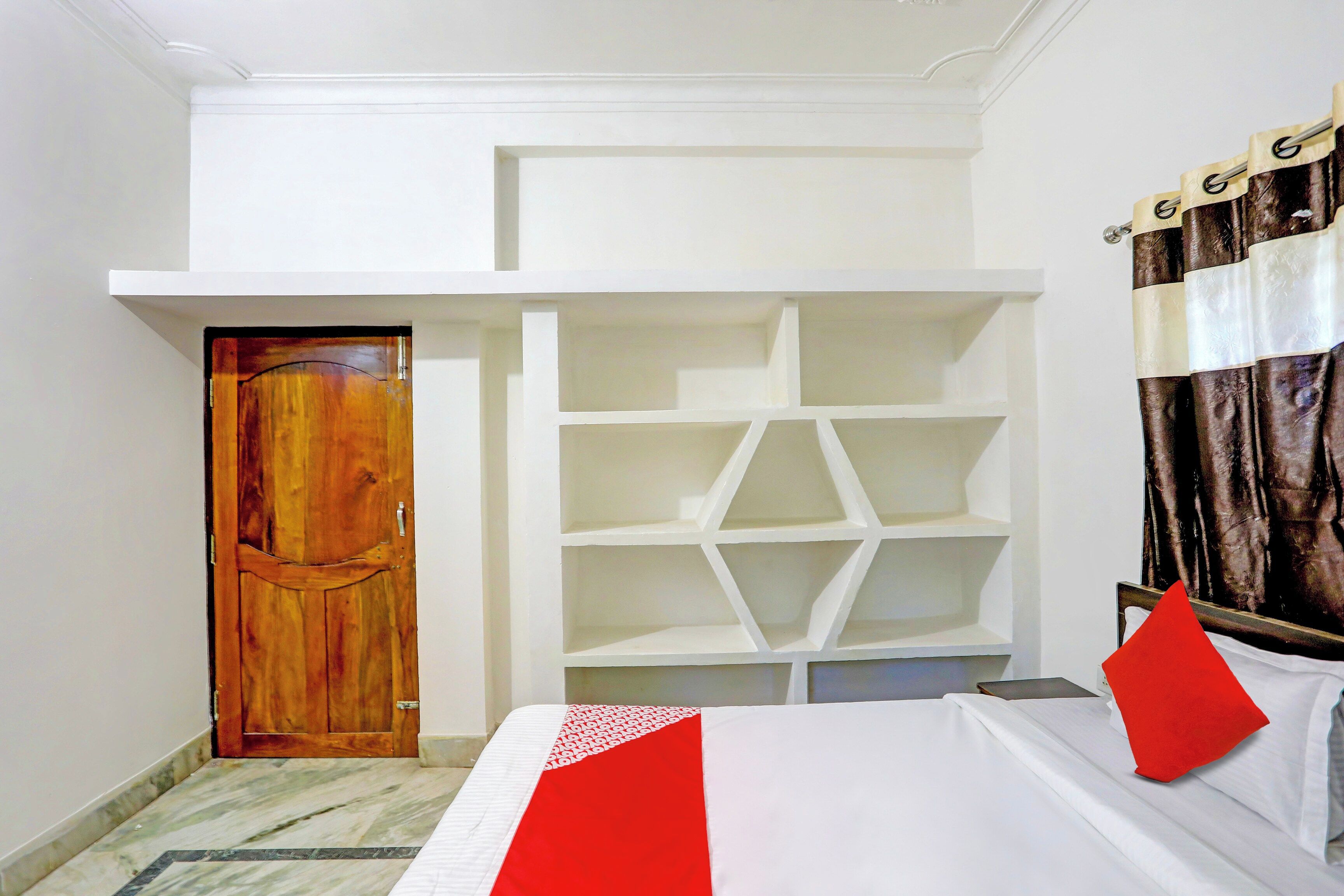 Habitación de hotel con cama, armario con varios estantes, puerta de madera y cortina.