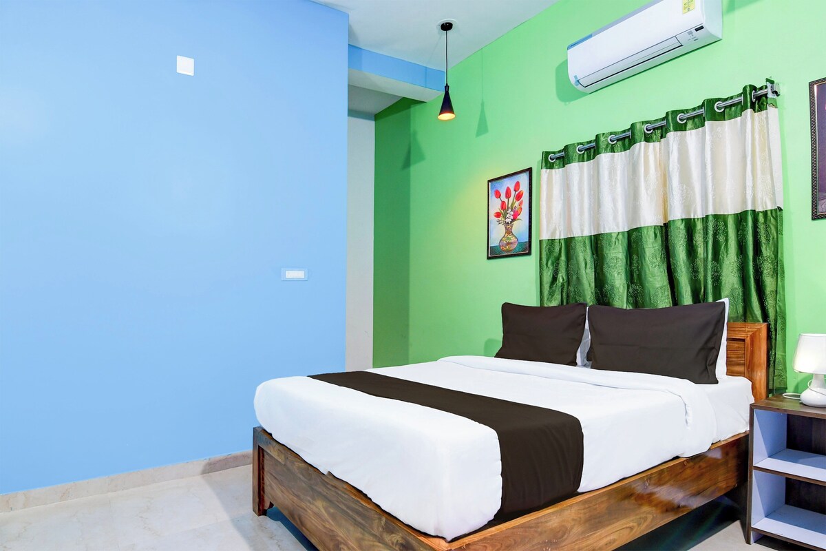 Un dormitorio con cama, mesita de noche, lámpara, un cuadro y ventana con cortinas.