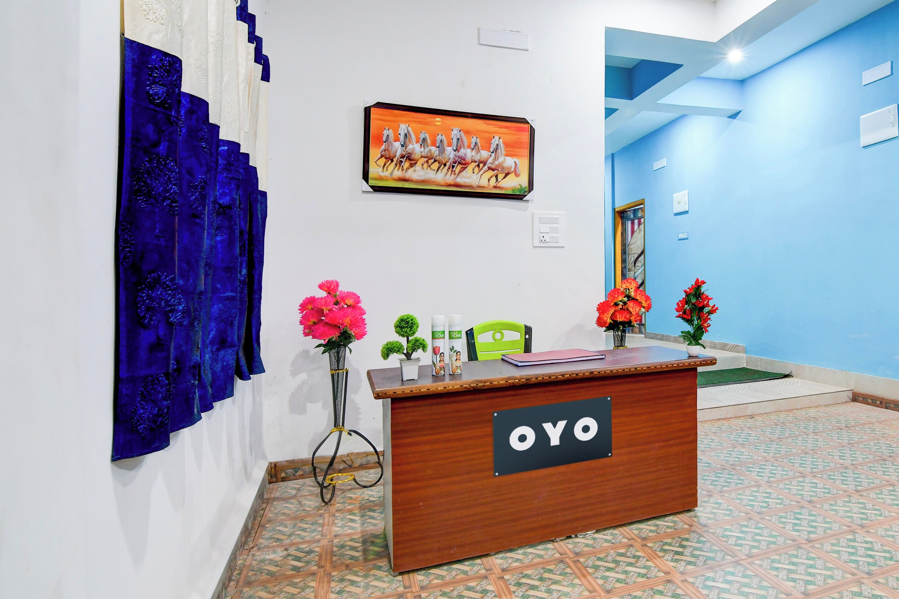 A reception desk with a sign reading 'OYO' in a hotel lobby with a blue wall and a painting of horses.