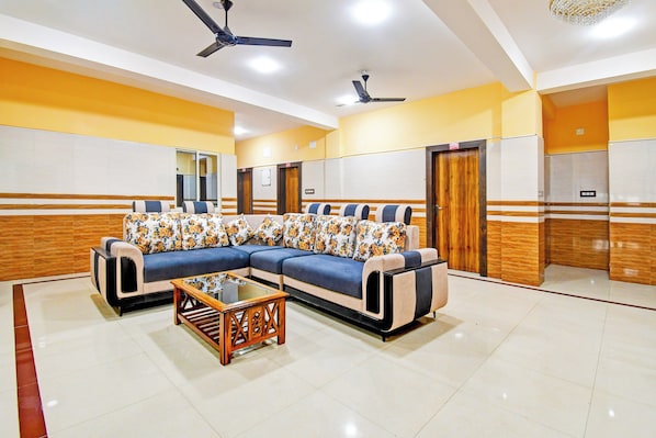 A hotel room with a sectional sofa, a wooden coffee table, and a ceiling fan.