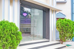 A building entrance with a glass door, steps leading up to it, and two small trees on either side.